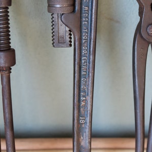Może przedstawiać: Zbliżenie na zardzewiały klucz do rur z wygrawerowanym tekstem "THE RIDGE TOOL CO. ELYRIA OHIO U.S.A. 1/8". Klucz ma oznaczenie rozmiaru 3,2 mm.