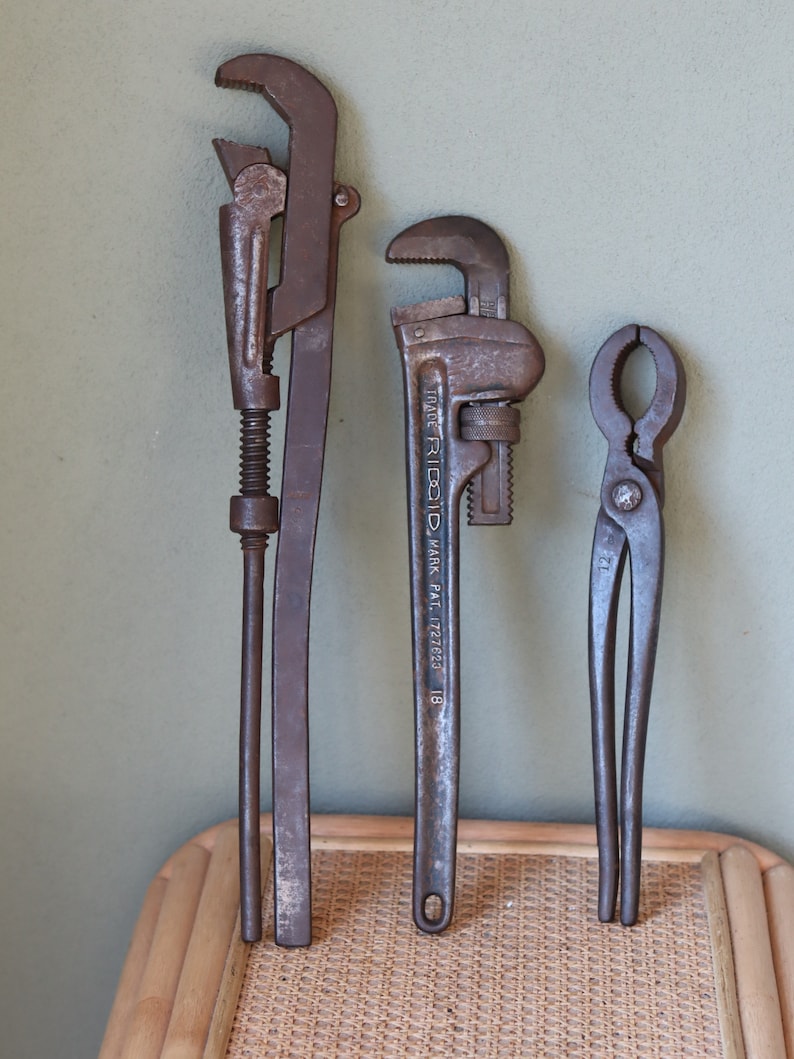 Może przedstawiać: Trzy stare, zardzewiałe metalowe klucze, dwa to klucze do rur, a jeden to szczypce. Klucze do rur mają napis "TRADE RIDGID MARK PAT. 1727223 18".