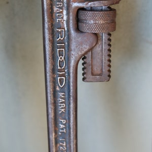 Może przedstawiać: Zbliżenie na zardzewiały klucz do rur z napisem "TRADE RIDGID MARK PAT. 1727623" na uchwycie.