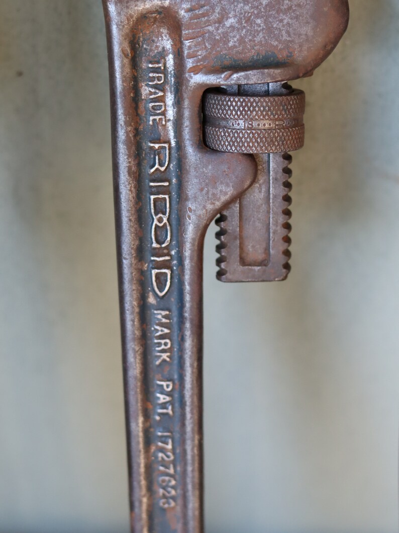 Może przedstawiać: Zbliżenie na zardzewiały klucz do rur z napisem "TRADE RIDGID MARK PAT. 1727623" na uchwycie.