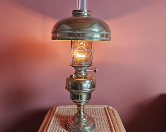 May include: A brass oil lamp with a glass shade and a clear glass chimney. The lamp is lit and casting a warm glow.