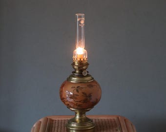 May include: A vintage oil lamp with a brown glass globe decorated with a floral pattern. The lamp has a brass base and a glass chimney.