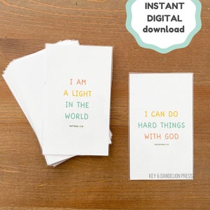May include: Two printable cards with inspirational quotes and bible verses. The first card is white with the text "I am a light in the world" and the bible verse "Matthew 5:14". The second card is white with the text "I can do hard things with God" and the bible verse "Philippians 4:13". Both cards have a colorful design with a key and dandelion logo at the bottom.