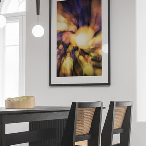 May include: Two black dining chairs with woven cane seats and backs, placed in front of a black table. A framed abstract art print with a blurred, colorful design hangs on the wall behind the table.