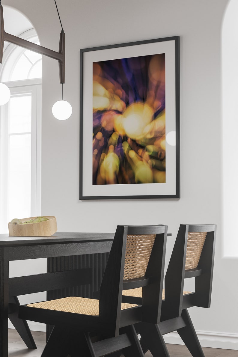 May include: Two black dining chairs with woven cane seats and backs, placed in front of a black table. A framed abstract art print with a blurred, colorful design hangs on the wall behind the table.