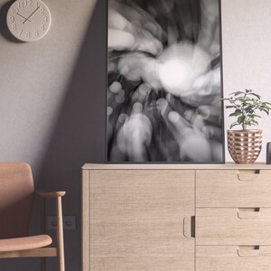 May include: A black and white photograph of a blurred city scene with a circular light source in the center. The photo is framed in a black frame and is hanging on a wall above a wooden dresser.