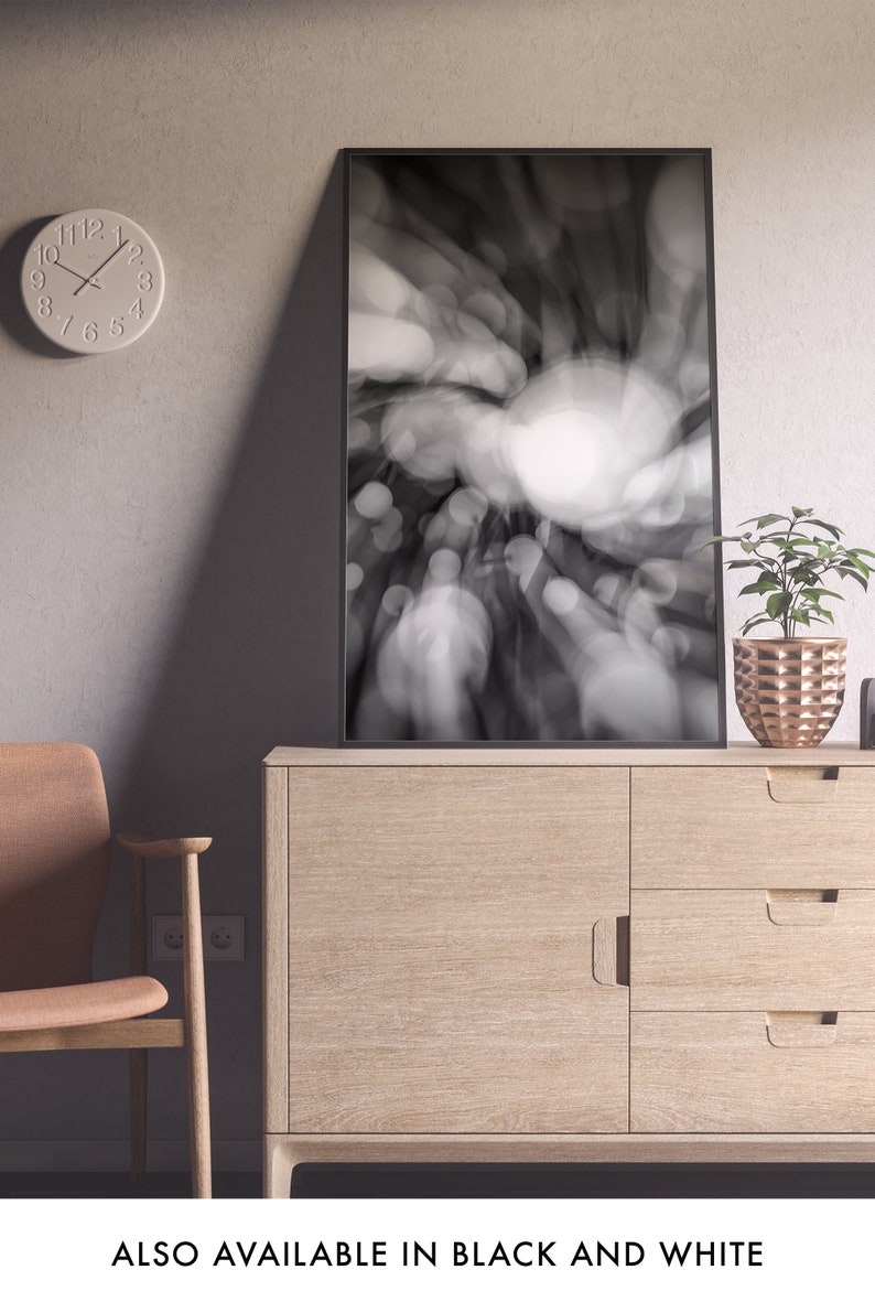 May include: A black and white photograph of a blurred city scene with a circular light source in the center. The photo is framed in a black frame and is hanging on a wall above a wooden dresser.
