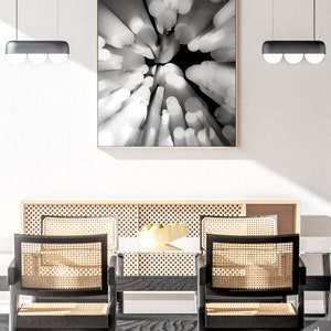 May include: A black and white abstract photograph of a circular pattern of light and dark shapes. The photograph is framed in a thin, wooden frame and is hanging on a white wall above a dining table with two chairs.