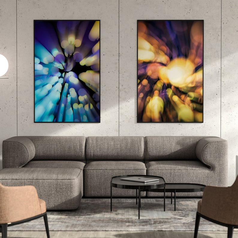 May include: Two abstract art prints with a blurred, colourful, and circular design. The prints are framed in black and hung on a grey concrete wall above a grey sectional sofa.
