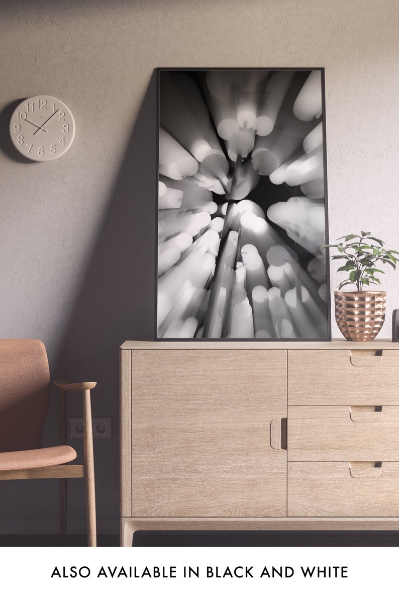 May include: A black and white photograph of a blurred abstract design with a circular pattern of light and dark shapes. The image is framed in a black frame and is hanging on a wall above a wooden cabinet.