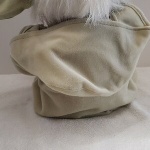 Op de afbeelding: Een pluche speelgoed van een groen personage met een witte bontkraag en een capuchon. Het speelgoed zit op een wit oppervlak.