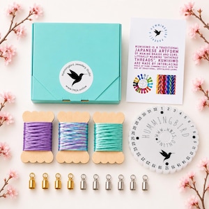 May include: A Kumihimo braiding kit with a teal box, spools of purple, blue, and teal cord, and gold and silver clasps. The kit includes a white disc with numbers and the text "Hummingbird" and "www.hbjs.online". A card explains Kumihimo.