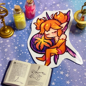 May include: A colorful sticker of a cartoon fairy with orange hair and wings, resting on a blue and white star-patterned surface. Miniature gold armillary sphere, compass, and bottles with glitter and a small open book are also present.