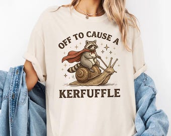 Camiseta Comfort Colors® Off to Cause a Kerfuffle, camiseta de mapache montando un caracol, humor con memes de animales, ropa sarcástica sobre salud mental.