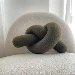 Könnte beinhalten: Ein grünes, geknotetes Kissen auf einer weißen, strukturierten Oberfläche.