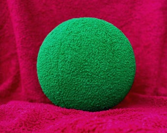 May include: A bright green, spherical decorative pillow with a textured, plush surface. The pillow is set against a vibrant fuchsia background, creating a striking contrast. The pillow's round shape and soft texture suggest comfort and style.