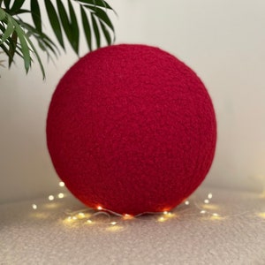 May include: A large, bright pink, fuzzy ball. The ball is sitting on a white surface with string lights around it.