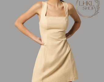 May include: A sleeveless, light beige linen dress with a square neckline and a fitted bodice. The dress has a slightly flared skirt and a simple, minimalist design.