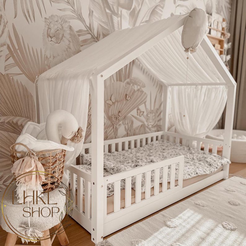May include: White canopy bed frame with a white and gray patterned mattress and a white swan stuffed animal. The bed is set against a wall with a tropical leaf pattern.