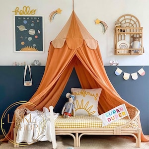 May include: A light orange canopy tent with a scalloped edge hangs over a yellow and white checkered bed with a wooden frame. The bed has a white throw blanket and a pillow with a sun and the word "minifairy" on it. There is a stuffed mouse wearing a blue and white striped shirt sitting on the bed. The bed is in a room with a blue wall and a wooden shelf with a rainbow and a stuffed bear on it.