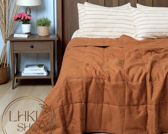 Könnte beinhalten: Ein Bett mit einer rostfarbenen, gesteppten Decke und gestreiften Kissen. Ein Nachttisch aus Holz mit einer Lampe, Büchern und einer Topfpflanze ist sichtbar. Das Bett steht vor einem hölzernen Kopfteil.