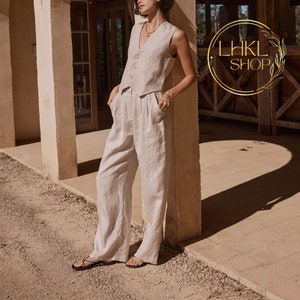 May include: A woman wearing a light brown linen vest and matching wide-leg pants. She is standing next to a pillar and has her hand in her pocket.