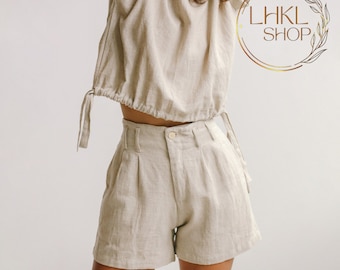 May include: A beige linen top with a gathered neckline and a matching pair of high-waisted linen shorts. The shorts have a button and zipper closure and pleats in the front.