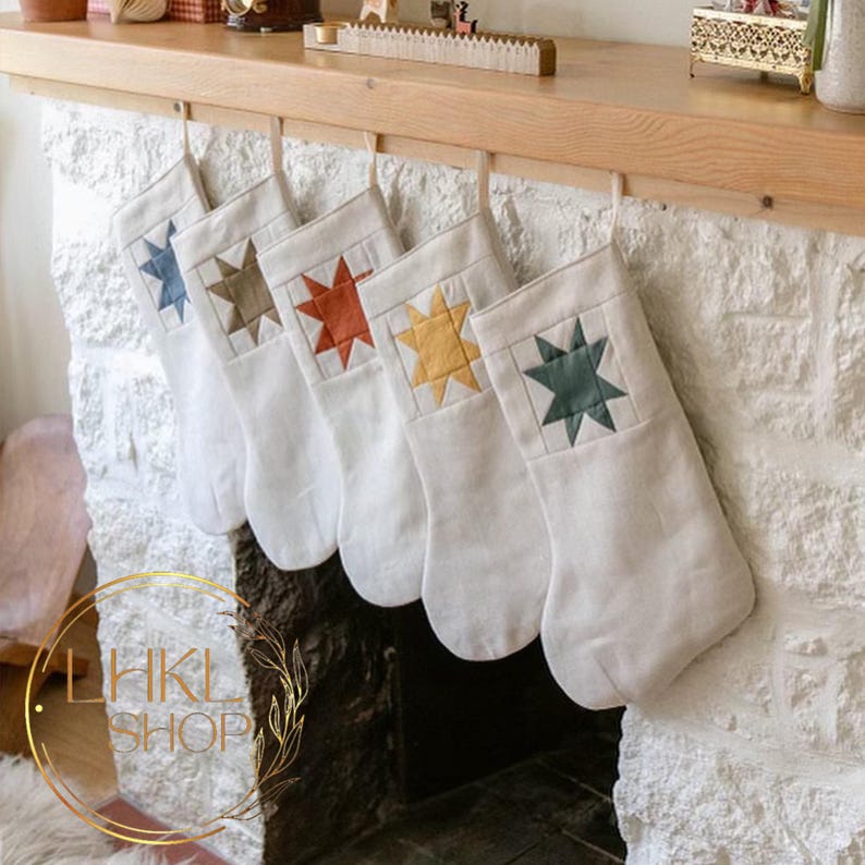 K&ouml;nnte beinhalten: F&uuml;nf wei&szlig;e Weihnachtsstr&uuml;mpfe mit verschiedenen Sternendesigns in Farbe. Die Sterne sind gr&uuml;n, rot, gelb, braun und blau. Die Str&uuml;mpfe h&auml;ngen an einem Holzmantel.