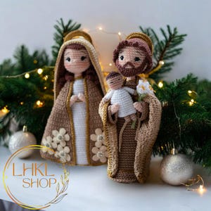 Könnte beinhalten: Gehäkelte Krippenszene mit Maria, Josef und dem Jesuskind. Die Figuren tragen braune und weiße Gewänder mit goldenen Akzenten und Heiligenscheinen. Maria hat einen braunen Schleier und Josef hält das Jesuskind und eine weiße Blume. Die Szene ist mit Weihnachtsschmuck und Grün geschmückt.