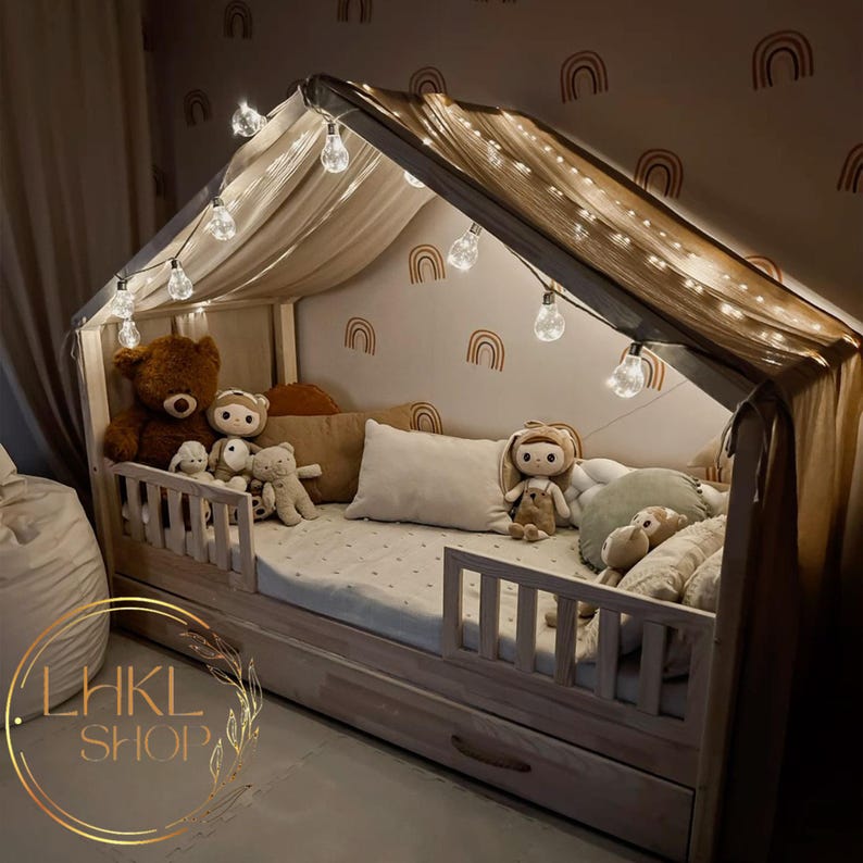 Pu&ograve; includere: Un lettino in legno per bambini piccoli con baldacchino e luci a catena. Il letto ha uno schema di colori bianco e marrone e dispone di un cassetto incorporato. Il letto &egrave; decorato con animali di peluche e cuscini.