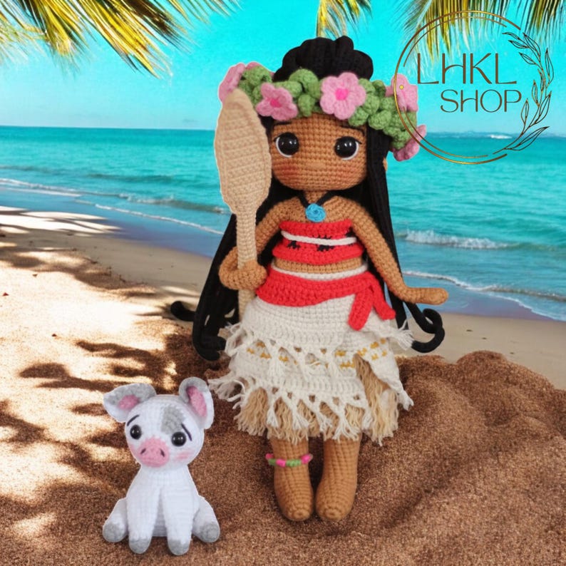 May include: A crocheted doll with brown hair wearing a flower crown and a red and white outfit, holding a wooden paddle. The doll is standing on a sandy beach with a small white crocheted pig beside it.