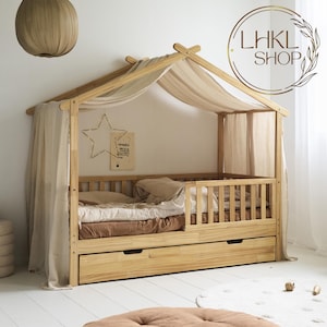 Puede incluir: Una cama de madera con dosel y un cajón debajo. La cama está hecha de madera natural y tiene un acabado marrón claro. El dosel está hecho de tela beige claro y está drapeado sobre el marco de la cama. La cama tiene un colchón blanco y una almohada blanca. La cama está en una habitación con paredes blancas y una alfombra marrón claro en el suelo.