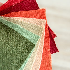 Puede incluir: Un conjunto de muestras de tela en varios tonos de rojo, naranja, beige, verde y verde claro. Las muestras están dispuestas en forma de abanico, con el tono más oscuro en la parte superior y el tono más claro en la parte inferior.