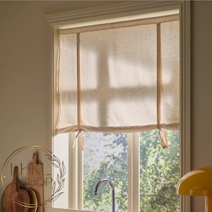 May include: A beige linen-look tie-up window curtain featuring two vertical fabric straps that allow the bottom edge to be gathered and secured at a desired height, covering the upper portion of a window frame with a soft, light-filtering fabric.