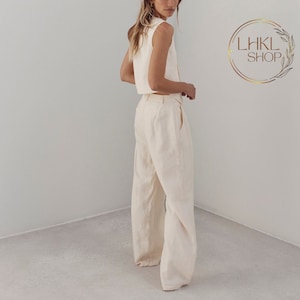 May include: A woman wearing a white sleeveless crop top and matching wide-leg pants. The pants have a high waist and a relaxed fit.
