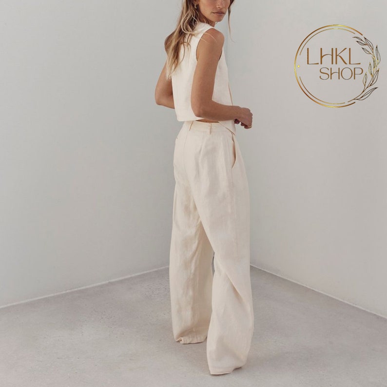 May include: A woman wearing a white sleeveless crop top and matching wide-leg pants. The pants have a high waist and a relaxed fit.