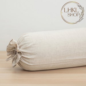 May include: A beige cylindrical bolster pillow made of linen fabric. The pillow has a gathered, ruffled end detail. The pillow is on a light wood surface. The logo "LHKL SHOP" is in the upper right corner.