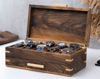 May include: A wooden watch box with a hinged lid and a pull-out drawer. The box is made of dark wood with a rich grain pattern. The lid is open and reveals multiple watch compartments. The box is sitting on a white surface.