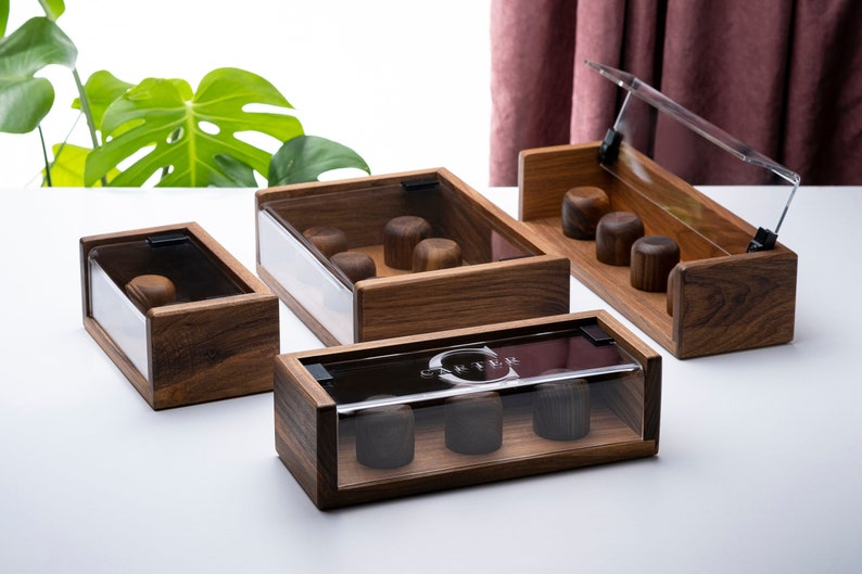 Puede incluir: Cuatro cajas de madera con tapas de vidrio transparente, cada una contiene peque&ntilde;os objetos redondos. Las cajas son de madera oscura y tienen un acabado natural. Las tapas son con bisagras y se abren para revelar el contenido.