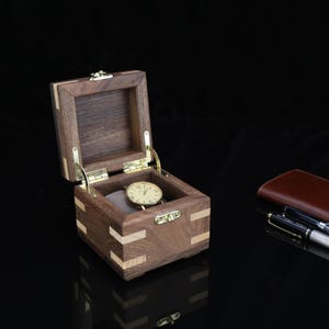 May include: A small wooden box with a hinged lid, made of walnut and maple wood, with a brass latch. The box is open and a watch is inside.