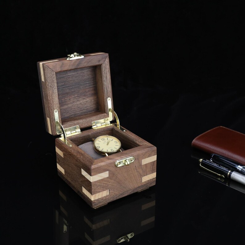 May include: A small wooden box with a hinged lid, made of walnut and maple wood, with a brass latch. The box is open and a watch is inside.