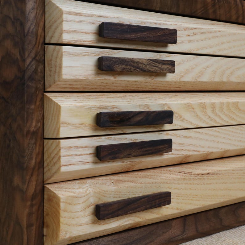 Puede incluir: Una caja de madera con cinco cajones, cada uno con un tirador de madera oscura. La caja est&aacute; hecha de madera clara y oscura.