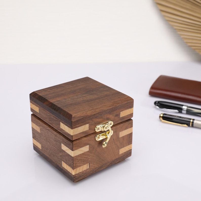 May include: A small wooden box with a hinged lid and a brass latch. The box is made of dark wood with light wood accents.