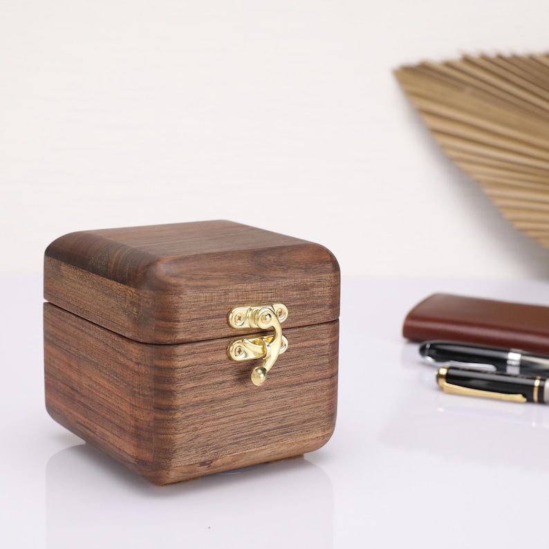 May include: A small, square wooden box with a hinged lid and a brass latch. The box is made of dark wood with a natural grain pattern.