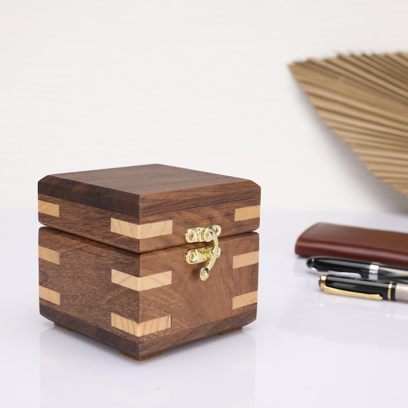 May include: A small wooden box with a hinged lid and a brass latch. The box is made of dark wood with light wood accents.