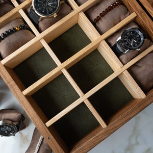 May include: A wooden watch box with multiple compartments for storing watches. The box is made of dark wood with a light wood interior. The compartments are lined with brown fabric and have a green felt bottom.