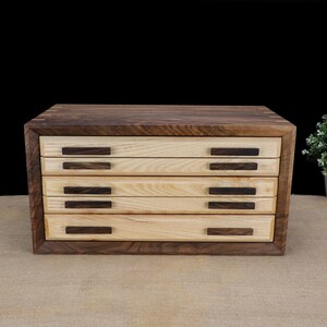 Puede incluir: Una caja de madera con cuatro cajones, cada uno con un tirador de madera oscura. La caja est&aacute; hecha de madera clara y oscura.