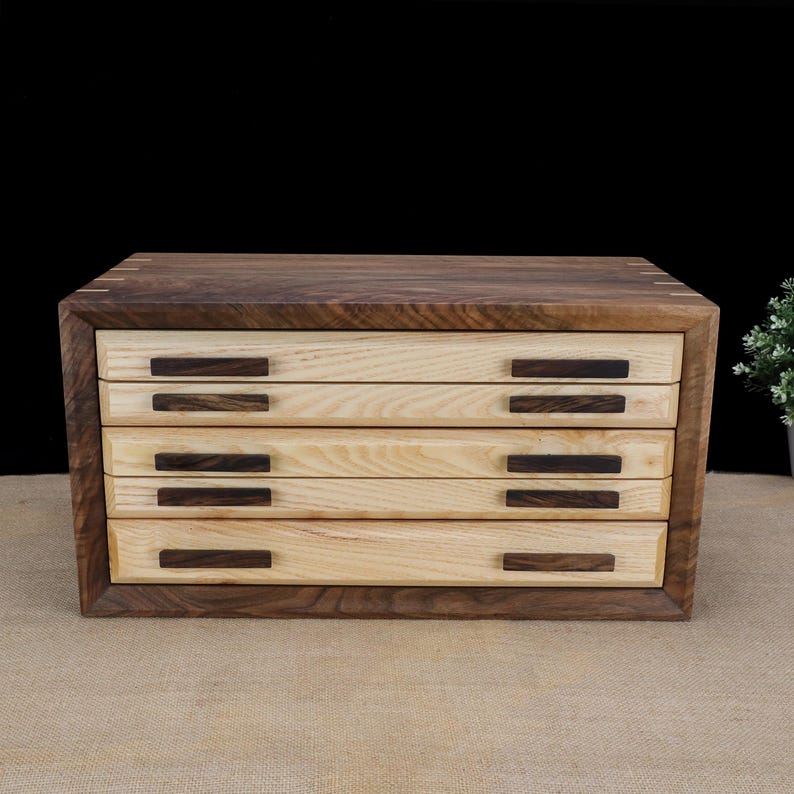Puede incluir: Una caja de madera con cuatro cajones, cada uno con un tirador de madera oscura. La caja est&aacute; hecha de madera clara y oscura.