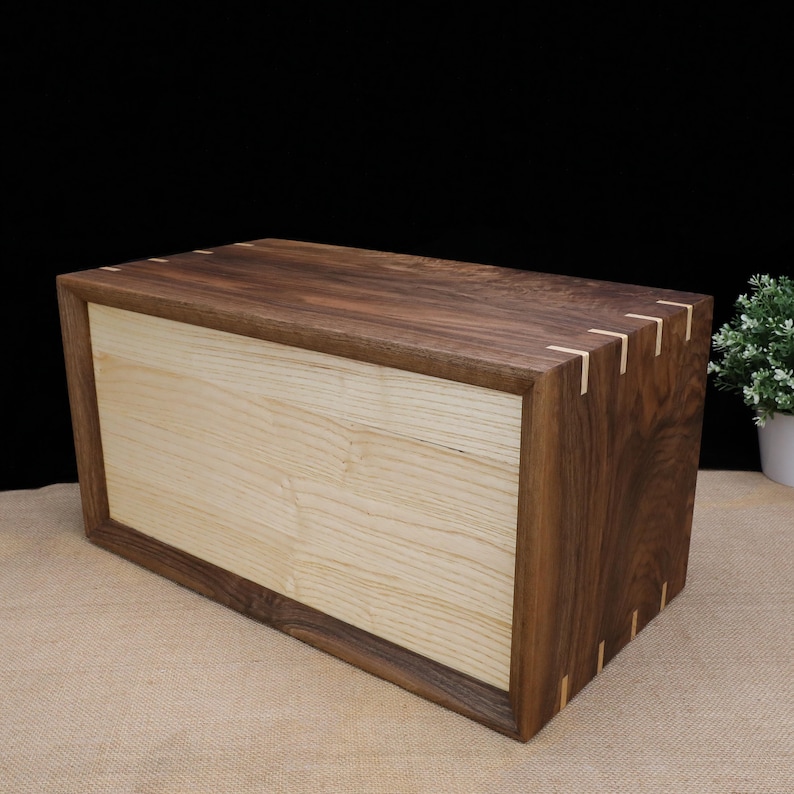 Puede incluir: Una caja de madera con un interior de madera clara y un exterior de madera oscura. La caja tiene un dise&ntilde;o simple con una forma rectangular y un acabado liso.