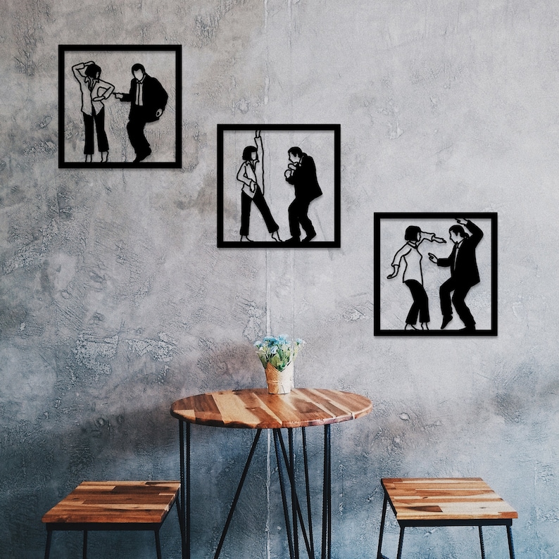 May include: Three black and white silhouette wall art pieces depicting a couple dancing. The art pieces are framed in black and hung on a gray concrete wall. A wooden table with a black metal frame sits in front of the wall art.